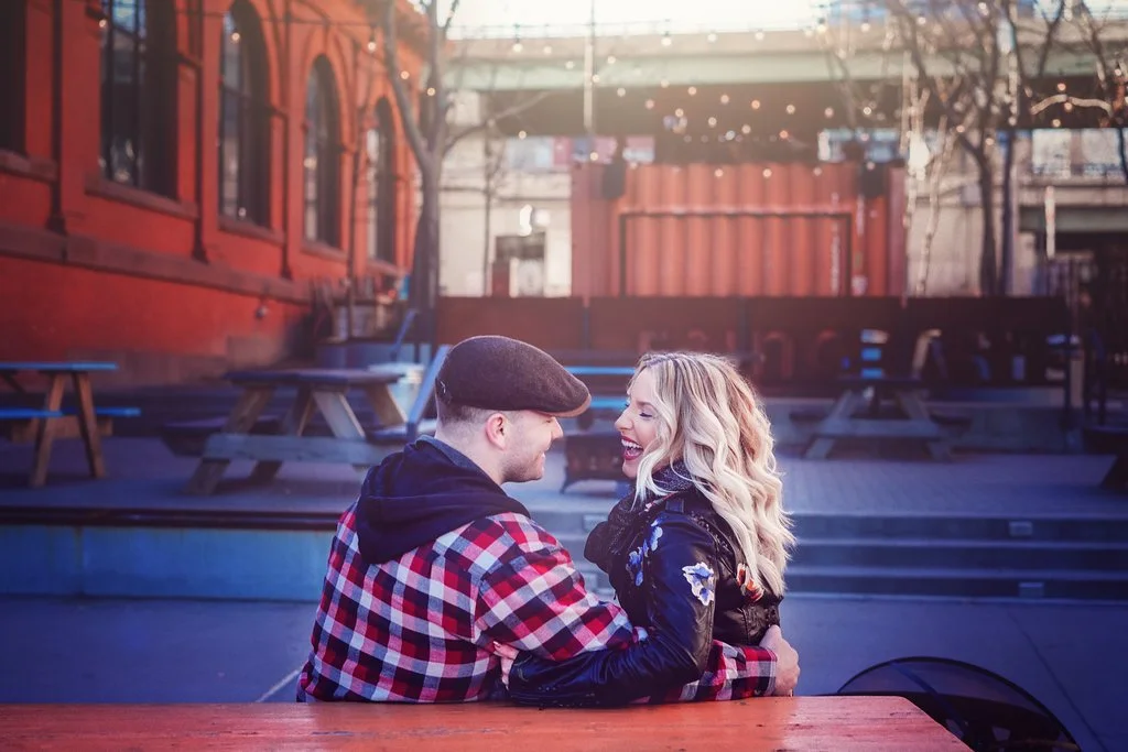 Engaged couple laughing together while sitting on a picnic table during their winter engagement session at Race Street Pier