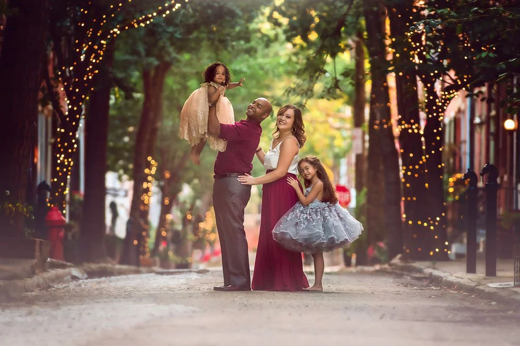 Family posing together and smiling during a relaxed portrait session on Addison Street in Philadelphia.