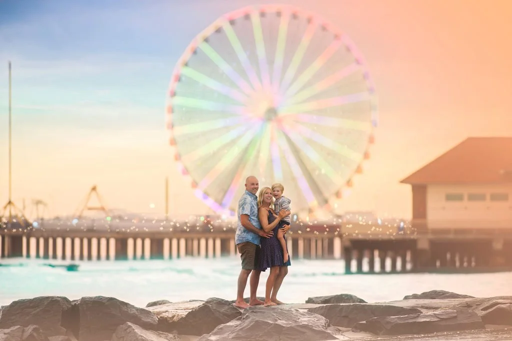 Family cuddled together on the beach in Atlantic City with the Ferris wheel at Steel Pier behind them.