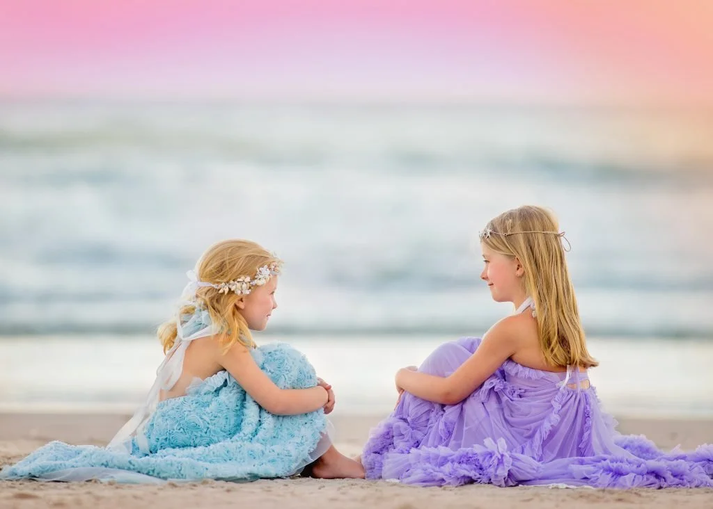 Two sisters sitting together on the sandy beach during a family portrait session in Ocean City, New Jersey along the Jersey Shore.