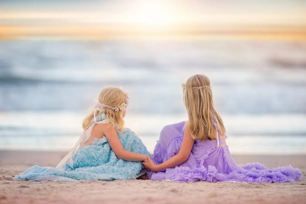 wo sisters holding hands while looking out at the ocean during a beach portrait session in Ocean City, New Jersey along the Jersey Shore.