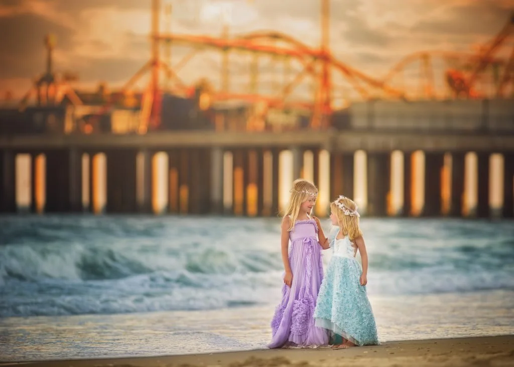 Two sisters looking at each other beside the ocean during a beach portrait session in Ocean City, New Jersey at the Jersey Shore.