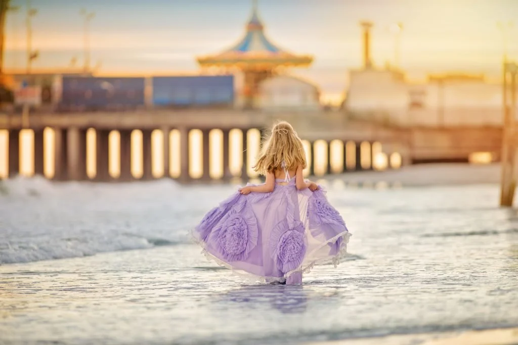 Young girl in a purple dress standing in the ocean during a beach portrait session in Ocean City, New Jersey along the Jersey Shore.