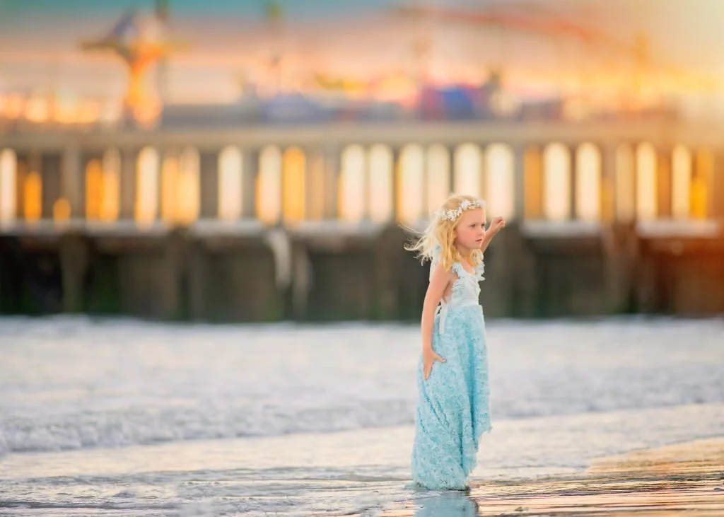 Young girl in a blue dress standing by the ocean water during a beach portrait session in Ocean City, New Jersey along the Jersey Shore.