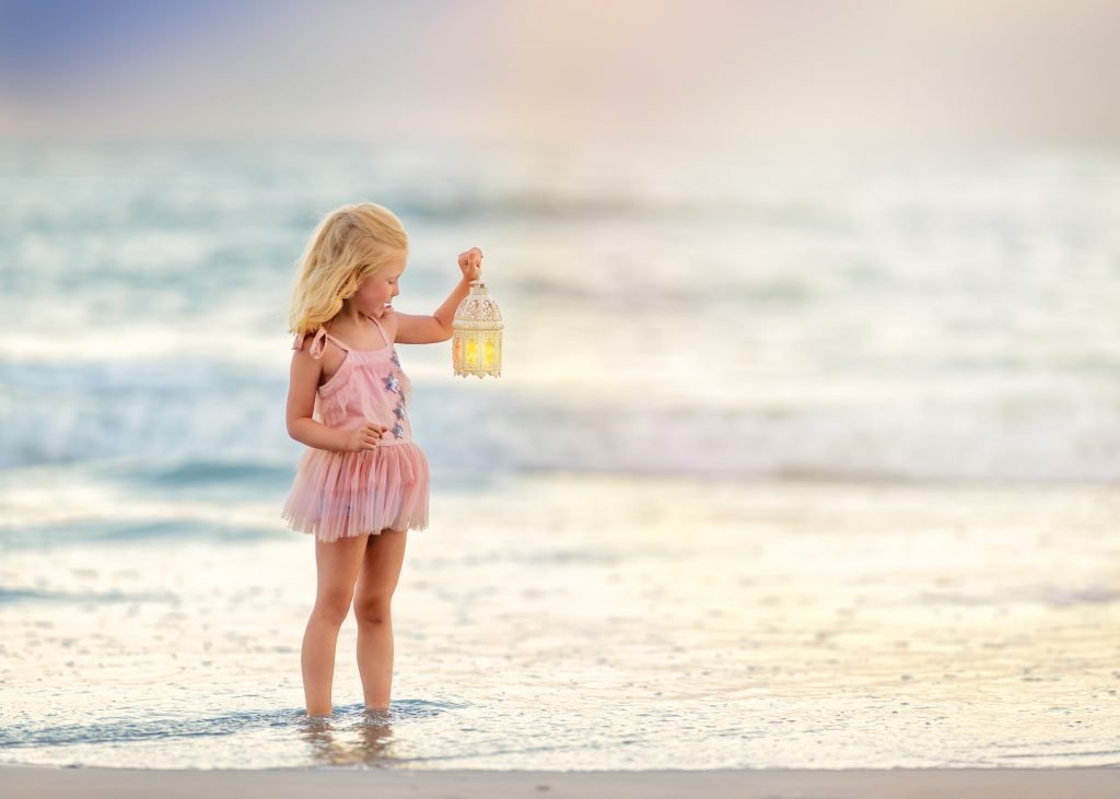Young girl in a pink dress holding a lantern by the ocean during a beach portrait session in Ocean City, New Jersey at the Jersey Shore.