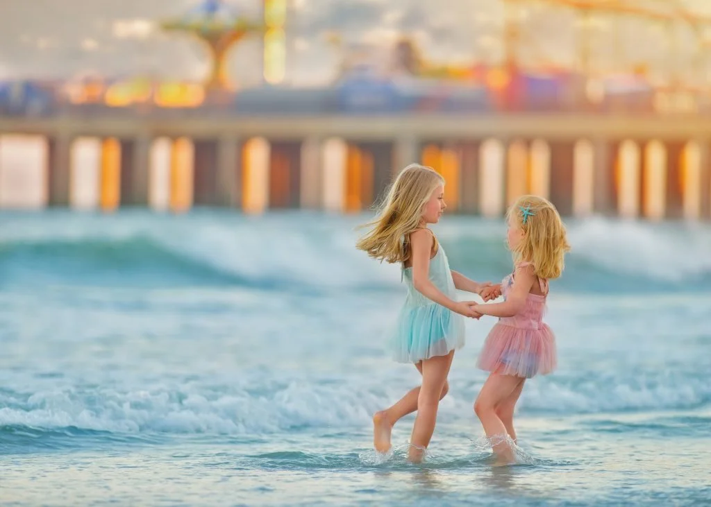 Two sisters twirling together beside the ocean during a dreamy beach portrait session in Ocean City, New Jersey at the Jersey Shore.