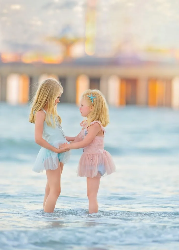 Two sisters holding hands while standing in the ocean during a beach portrait session in Ocean City, New Jersey at the Jersey Shore.