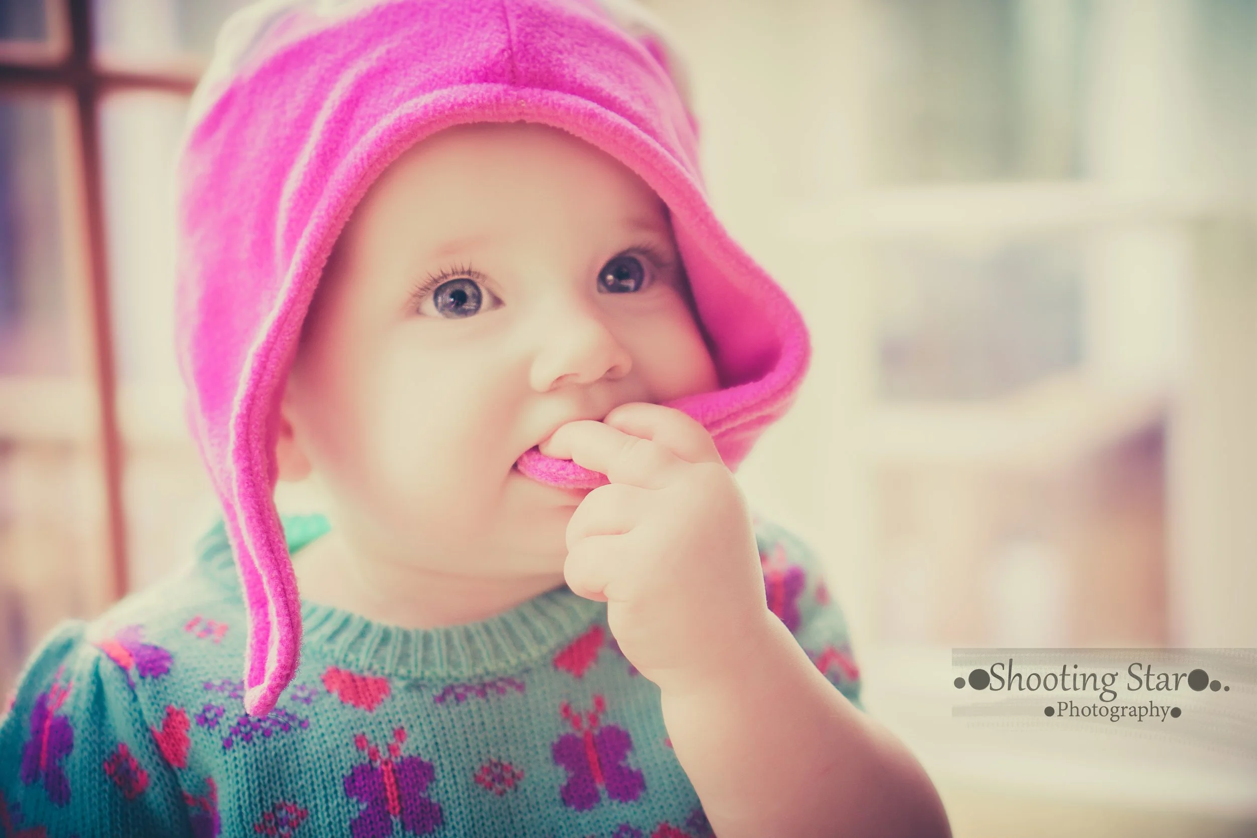 Baby chewing on her pink hat during a candid everyday moment.