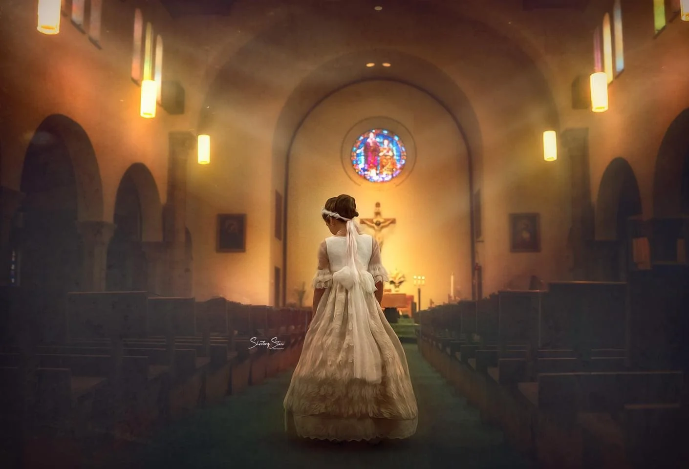 First Holy Communion portrait of a young girl standing in a church aisle, photographed from behind to highlight the back details of her Communion dress