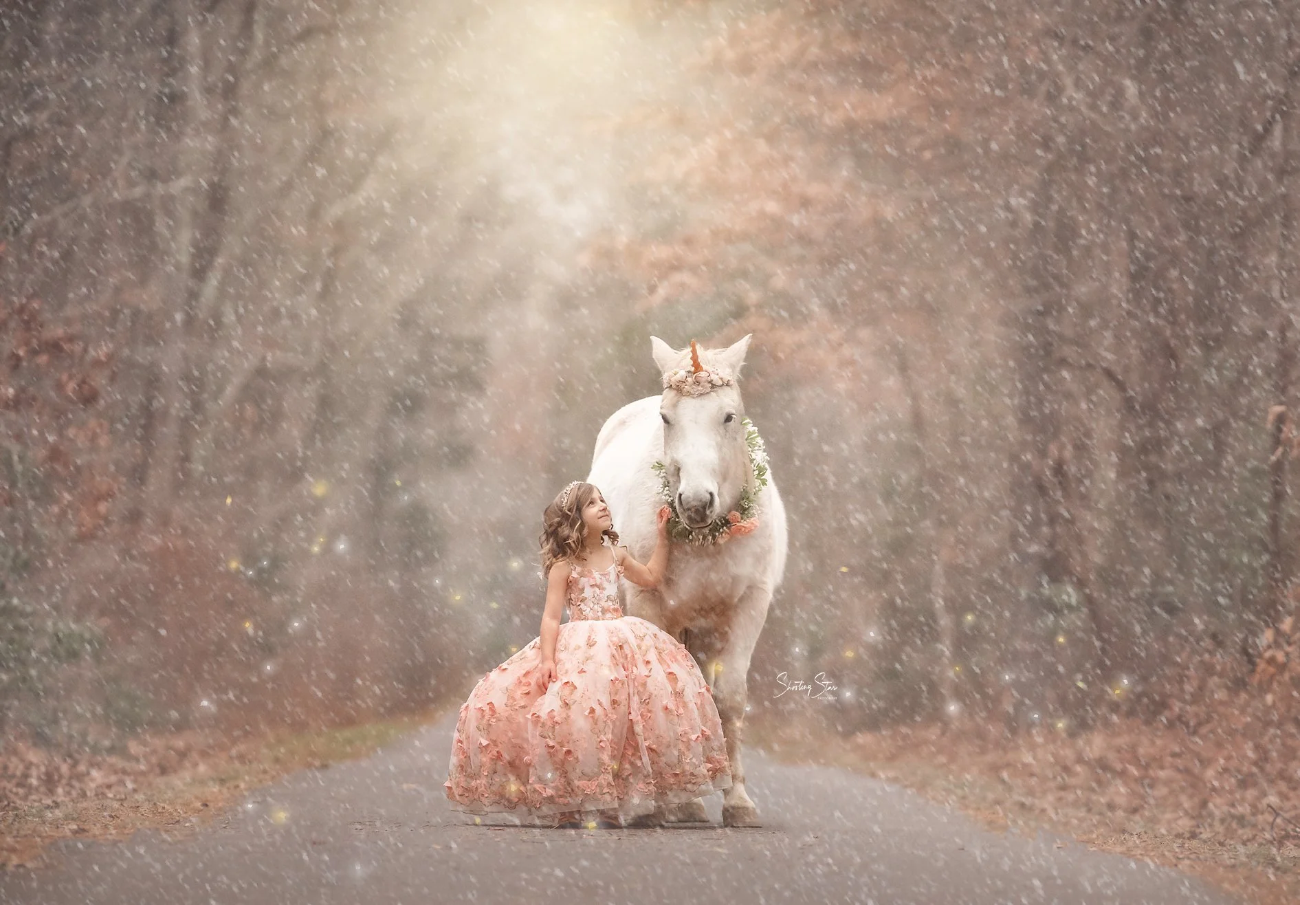 A smiling young girl gently holding Drifter the unicorn during a magical portrait session.