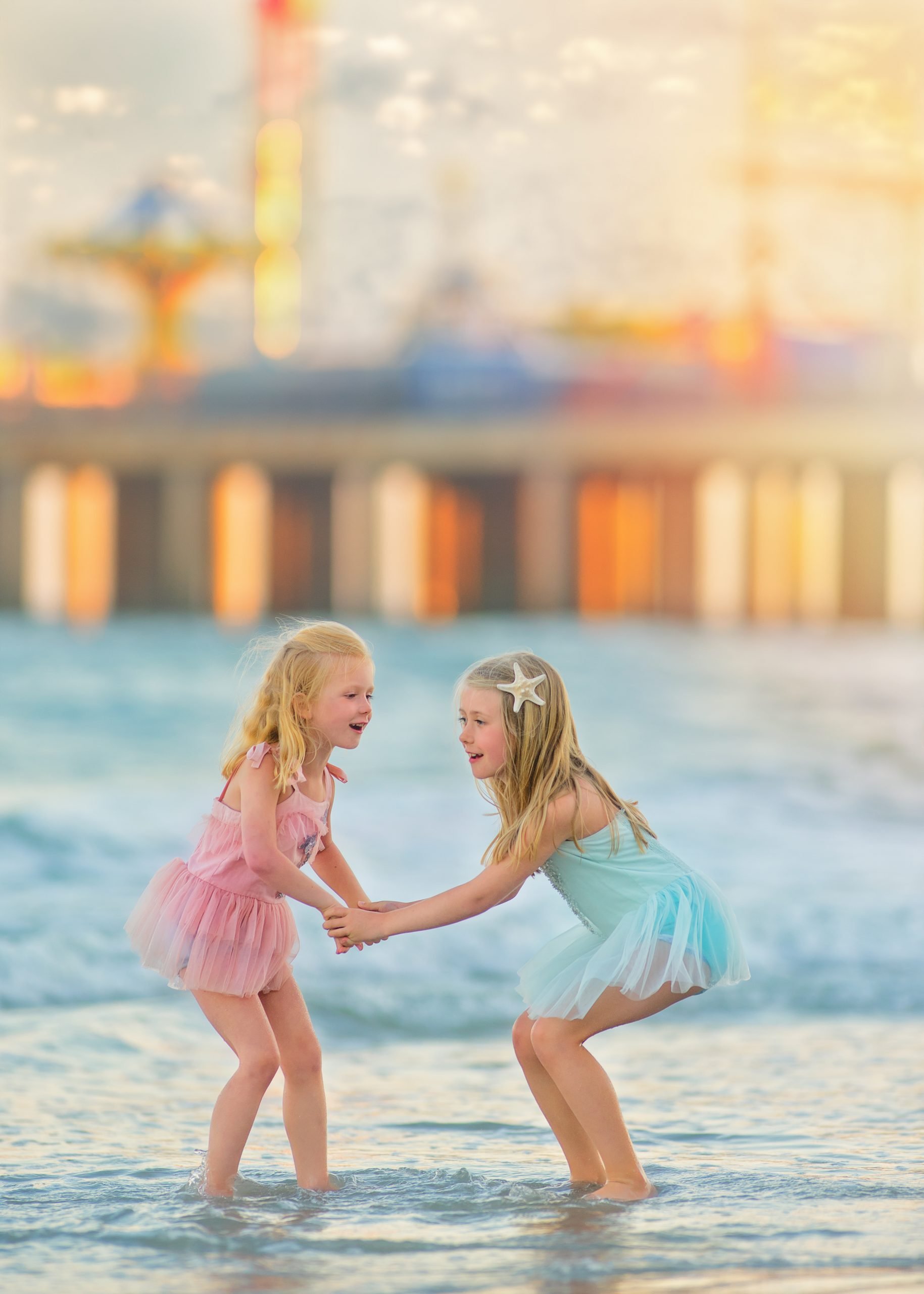 Two sisters laughing together while standing in the ocean water during a joyful beach portrait session in Ocean City, New Jersey at the Jersey Shore.