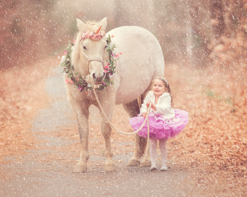 girl smiling in a pink couture dress beside a unicorn during a magical portrait session in New Jersey