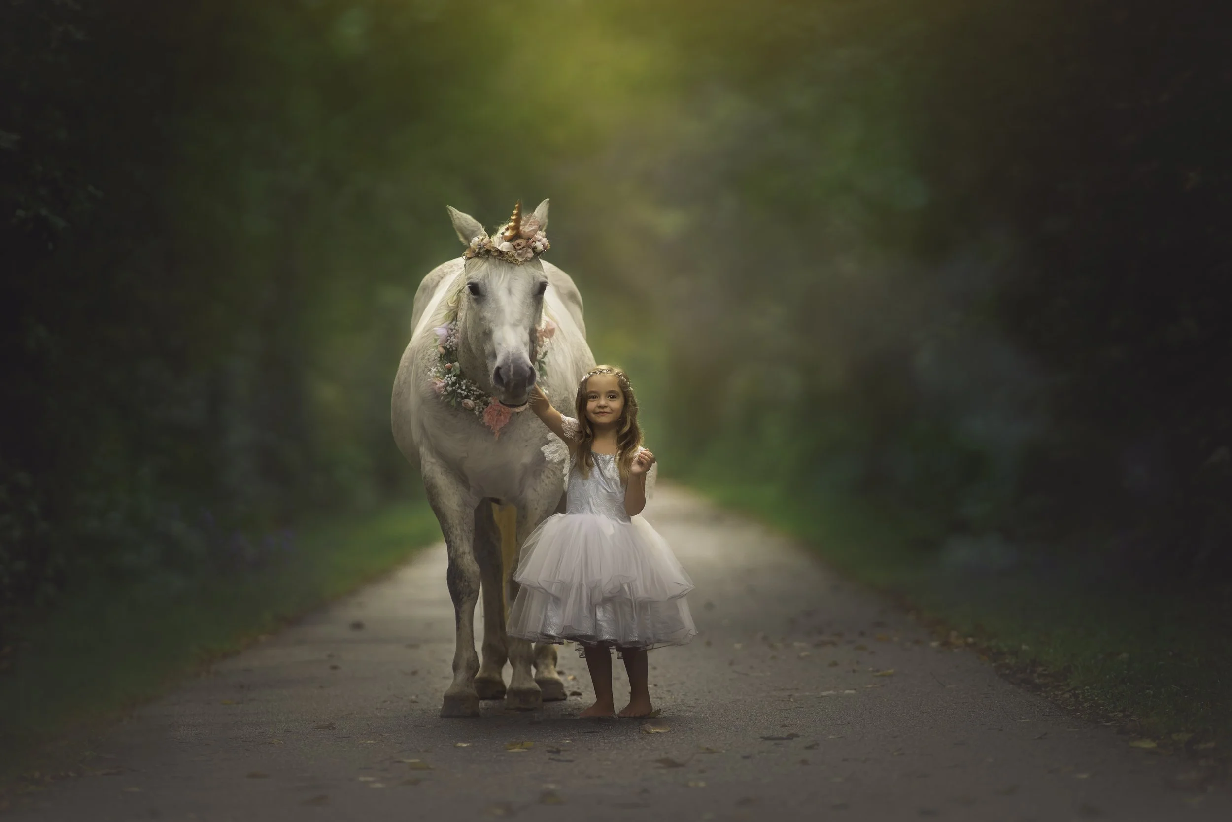 Little girl in a silver dress smiling at the camera beside a white unicorn during a South Jersey unicorn portrait session.