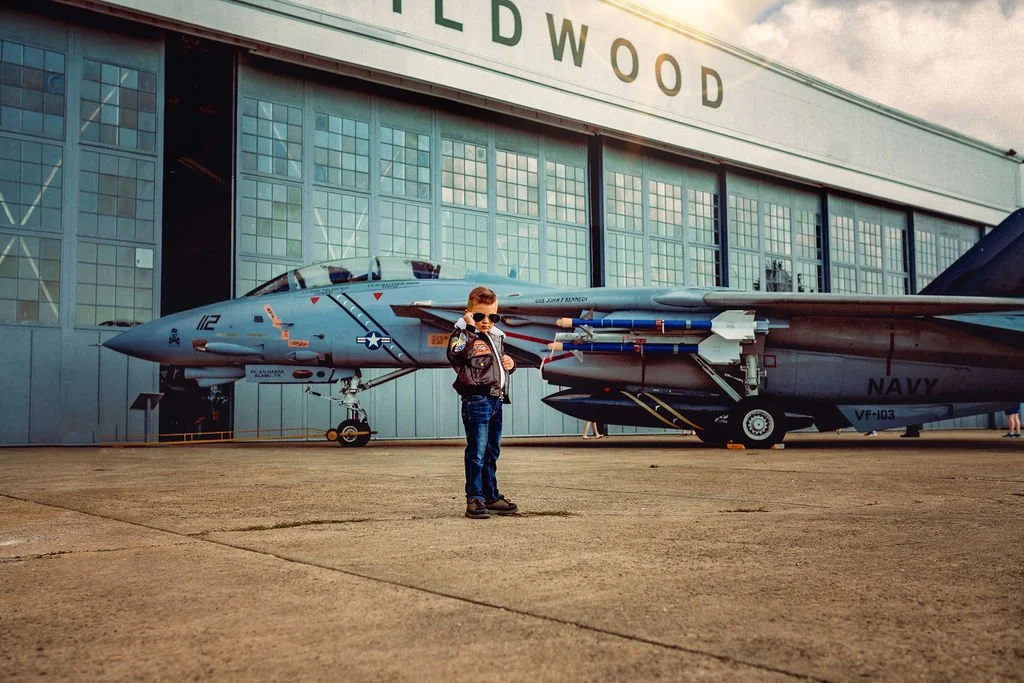 Wide shot of child in bomber jacket standing near jet during aviation photoshoot near Cape May New Jersey