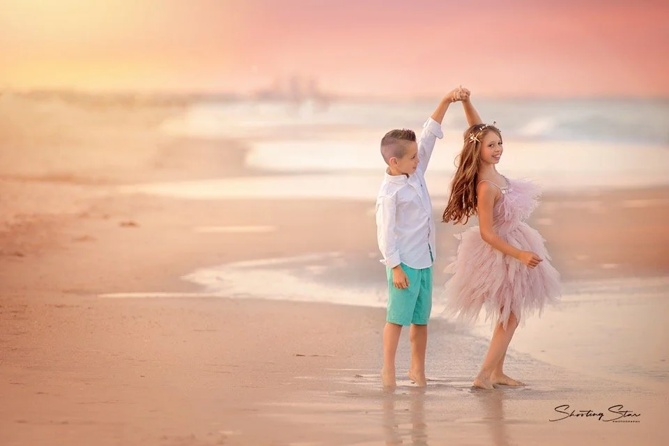 Brother and sister twirling together at the edge of the ocean during a Cape May family portrait session
