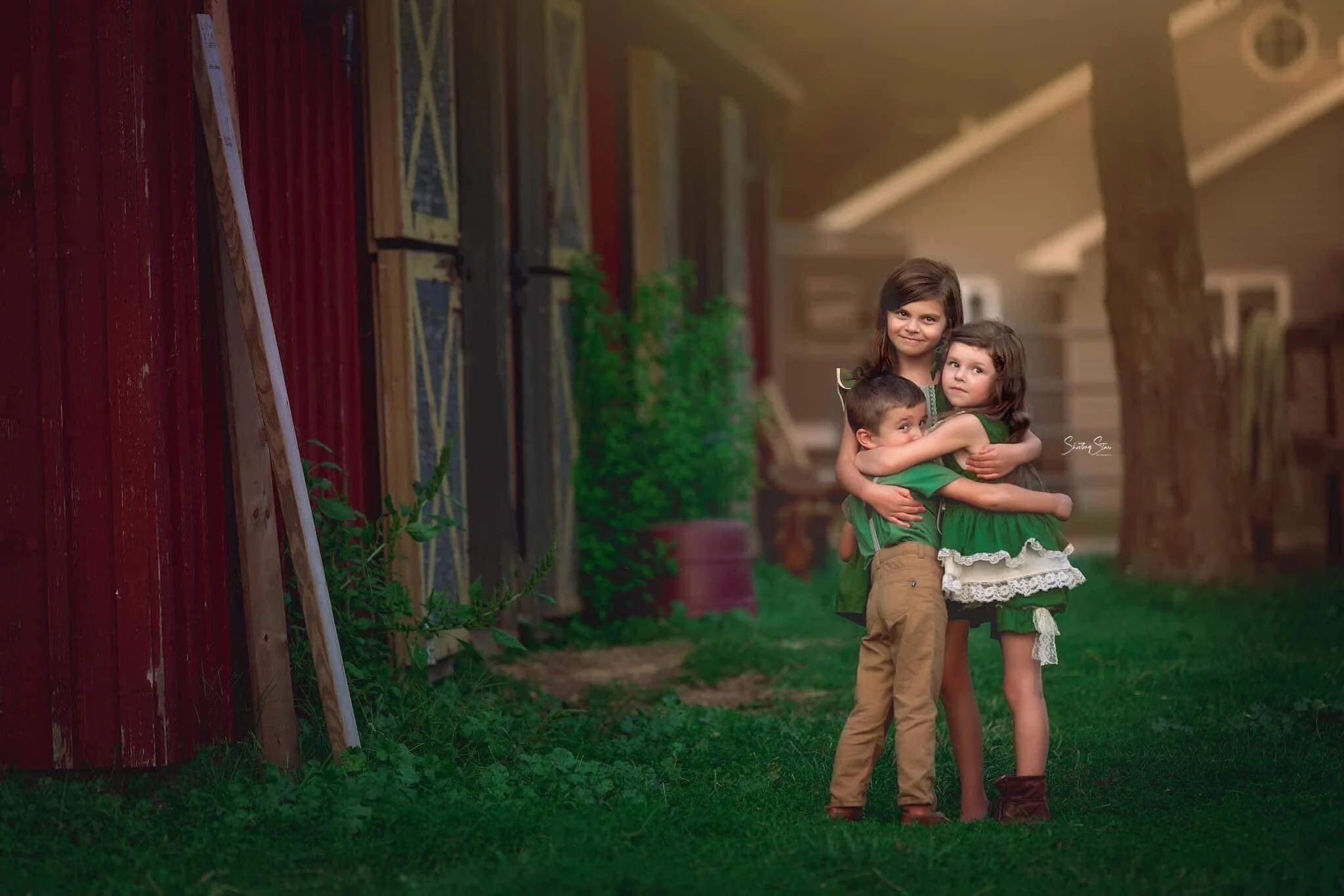 Siblings share a quiet hug in front of a rustic red barn during a fine art farm portrait session in South Jersey, surrounded by soft natural light and countryside textures.