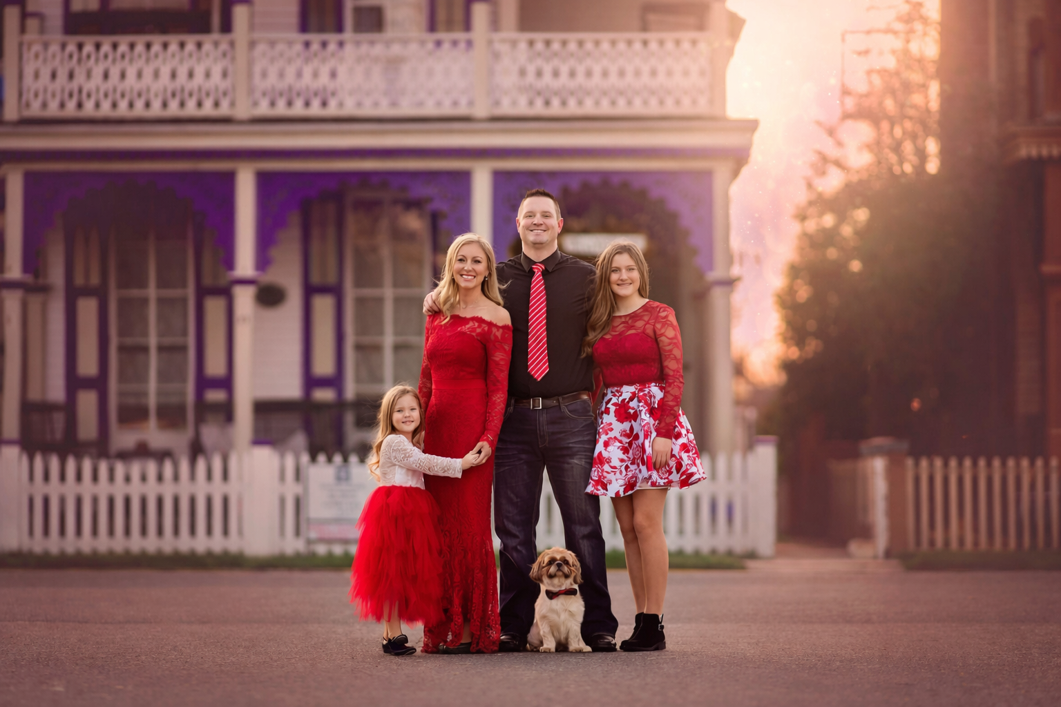 Family portrait of parents and children wearing red outfits in front of a historic Victorian home