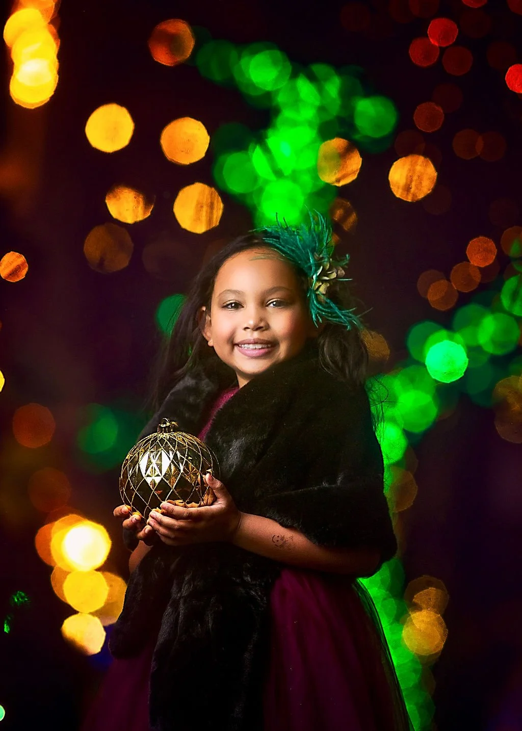 child holding ornament during Christmas portrait session with colorful lights background