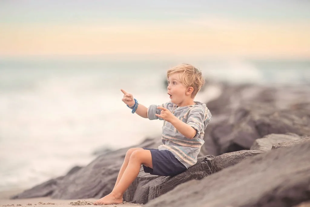 Little boy pointing at a seagull flying above the jetty during a family beach session in Atlantic City NJ.