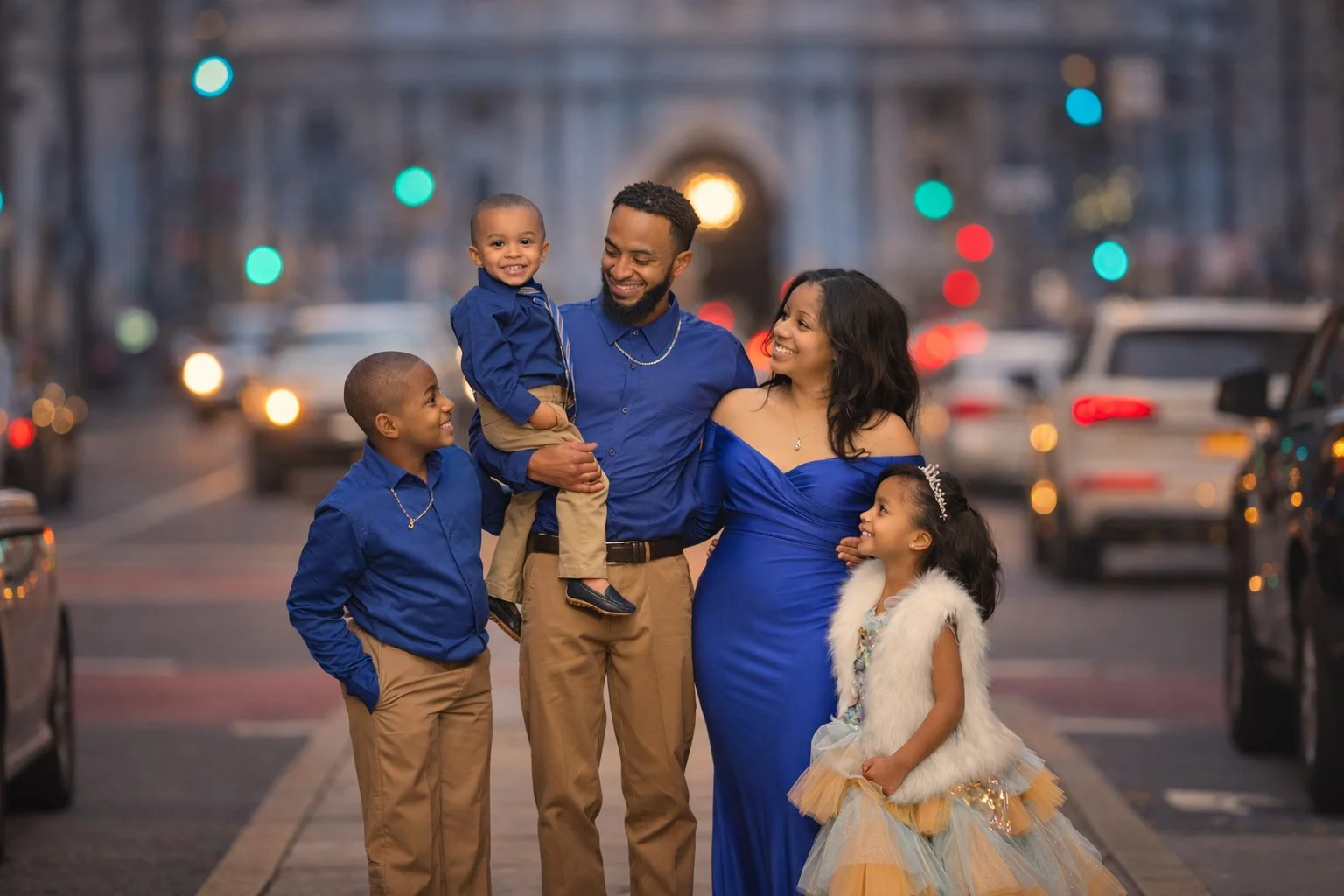 A family of five walking together on a Philadelphia city street at dusk, dressed in coordinated blue and neutral outfits during a natural fine art family portrait session.