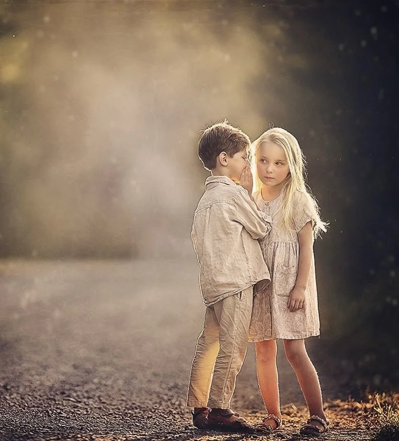 Two children share a soft whisper on a peaceful farm, captured in gentle natural light for a timeless fine art portrait that reflects connection and childhood curiosity in South Jersey.