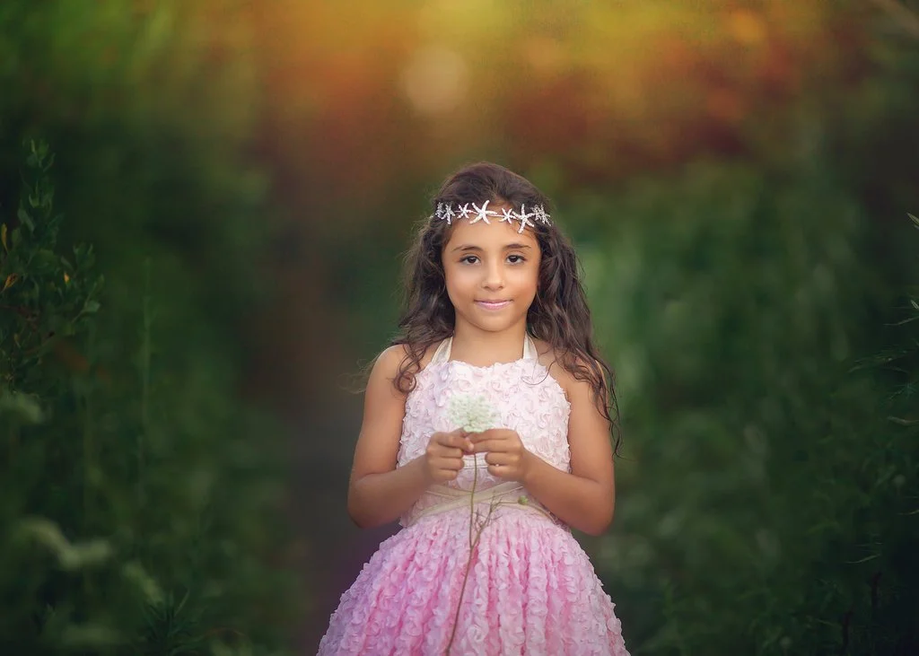 Up-close portrait of a little girl in a pink dress wearing a starfish crown at the Jersey Shore, captured during a magical birthday photo session in Cape May, NJ.