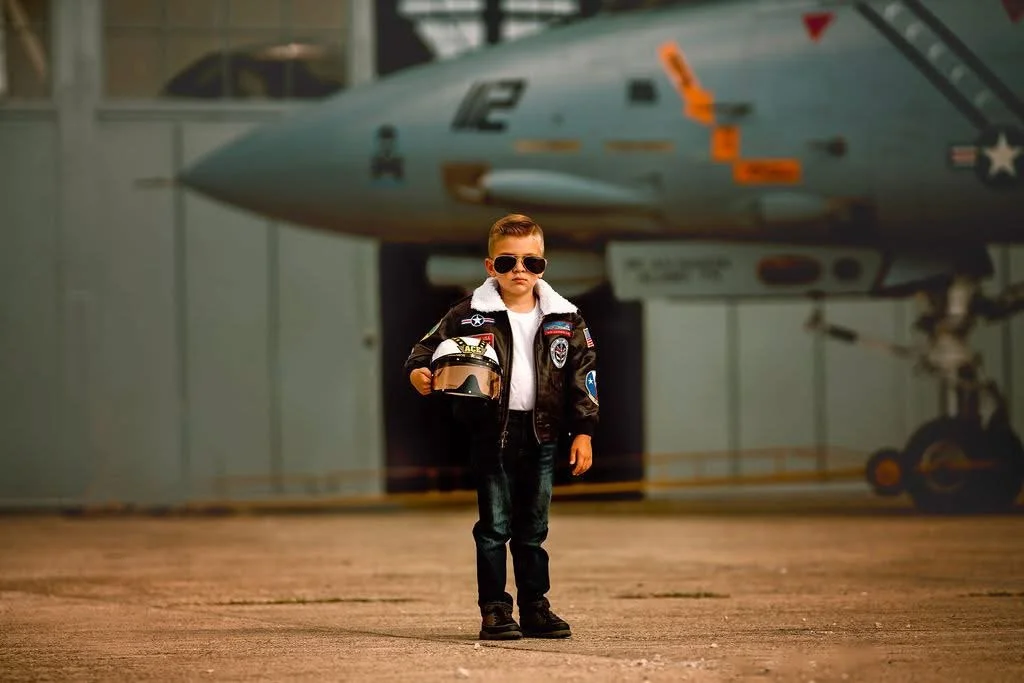 Boy wearing pilot helmet with serious expression posing in front of jet during aviation photoshoot near Cape May New Jersey