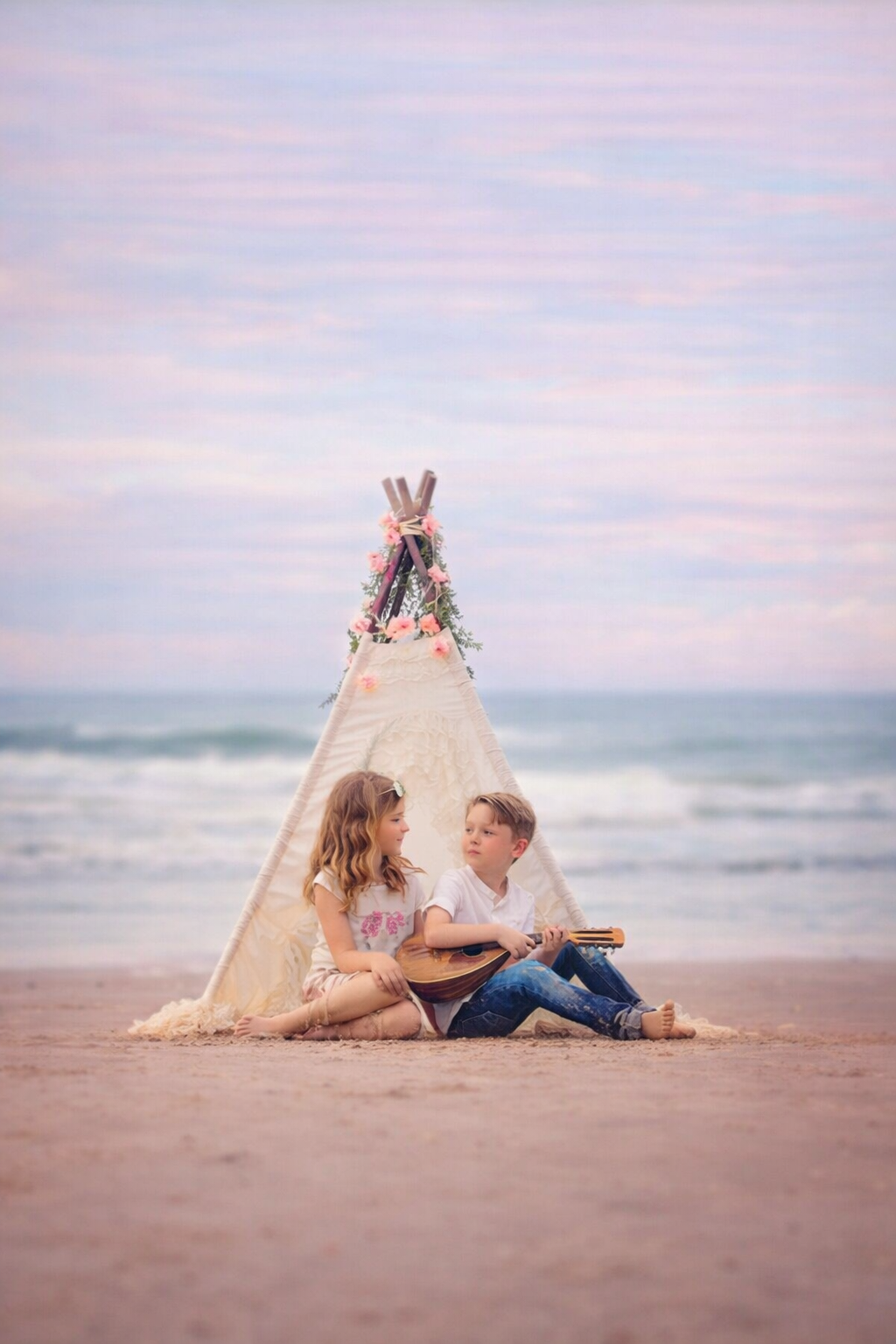 Two children playing guitar in front of a teepee during a Stone Harbor beach portrait session