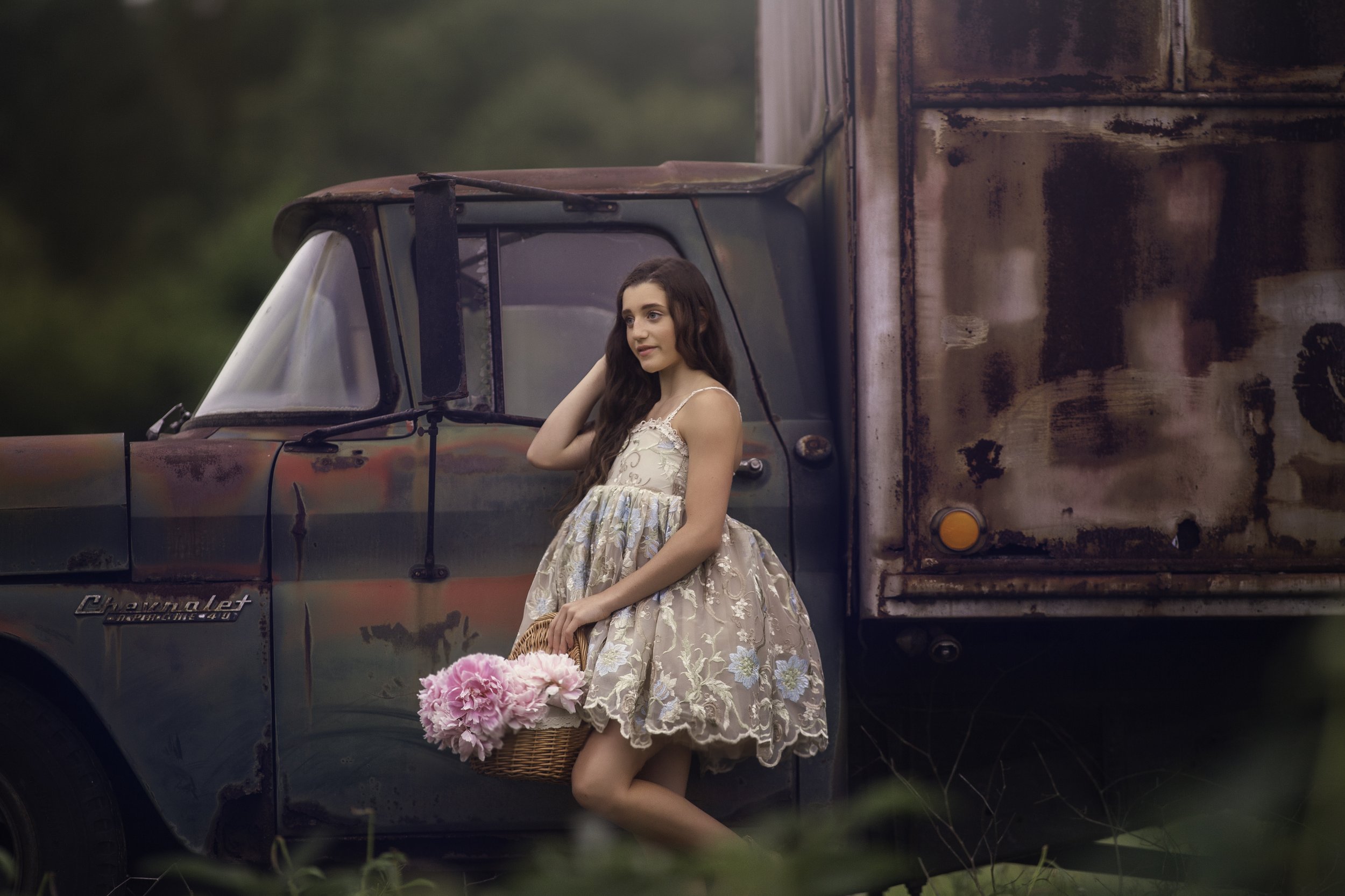 Fine-art teen portrait of a teenager posed with a rustic truck, featuring natural light and a timeless, editorial aesthetic.