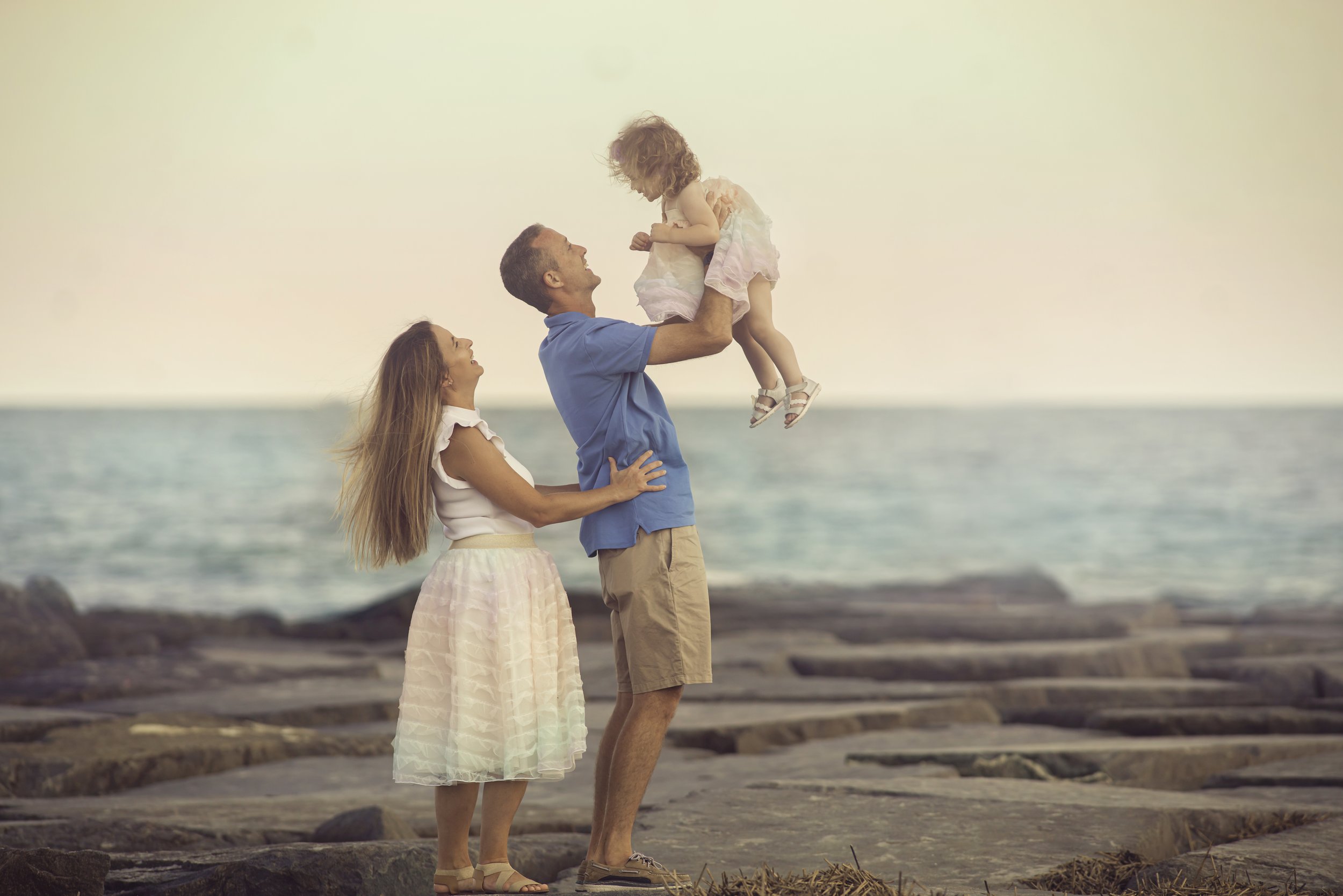 Mom, dad, and daughter standing together on a jetty during a Cape May family portrait session