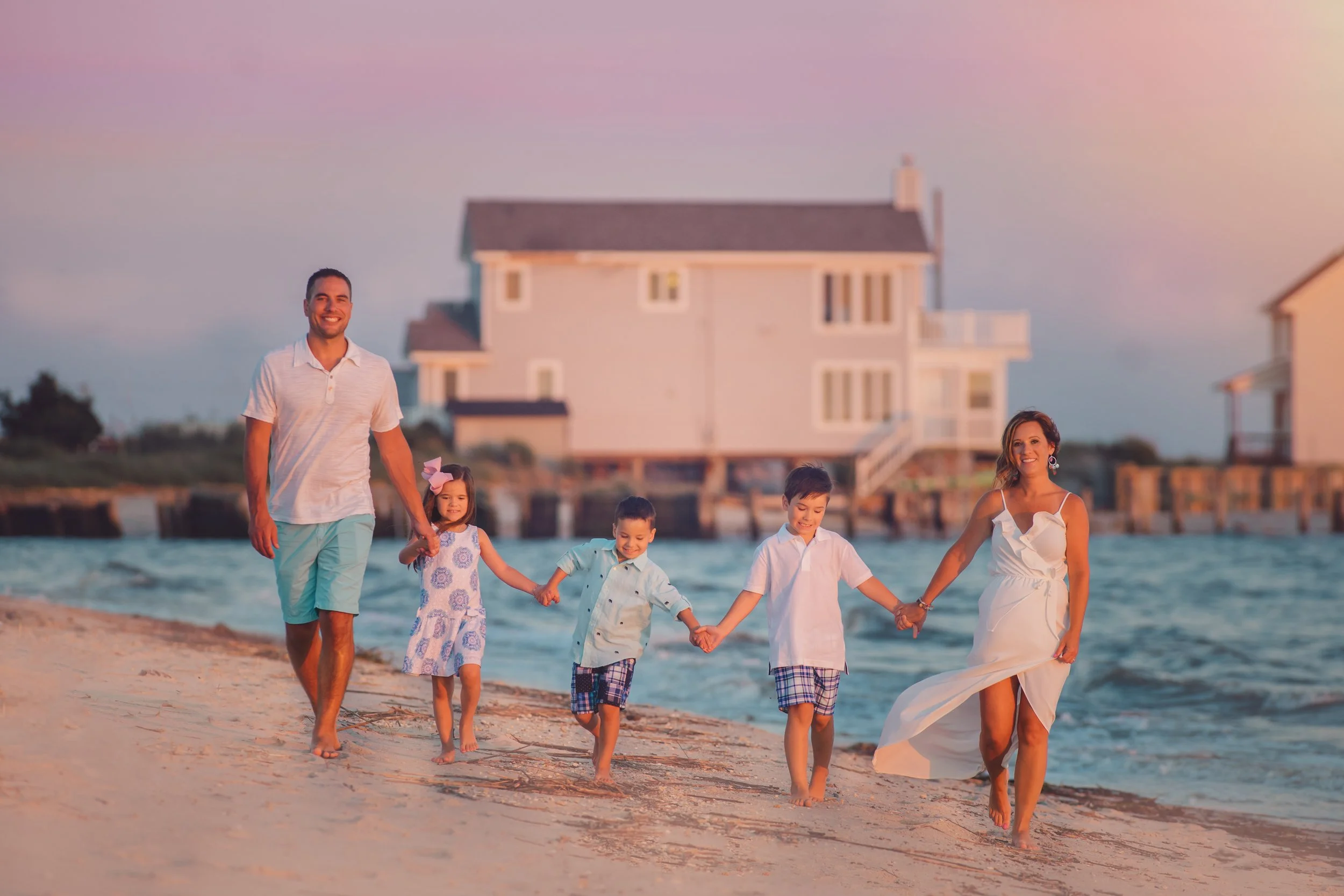 A family of five walks hand-in-hand along the shoreline at sunset, their connection and movement creating a relaxed, editorial beach portrait.