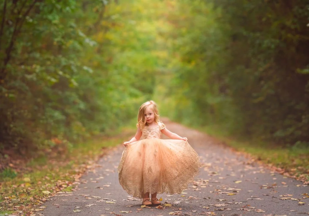 Young girl wearing a gold dress and holding an Anna Triant gown during a South Jersey maternity photography session.