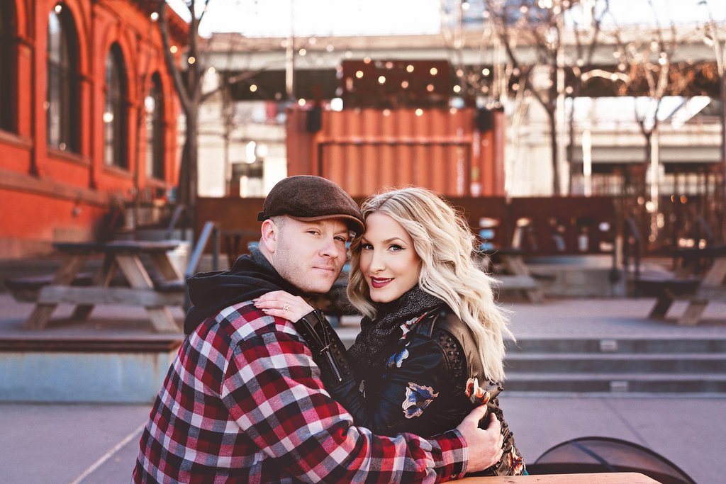 A wide view of an engaged couple seated at picnic tables during their engagement session at Race Street Pier