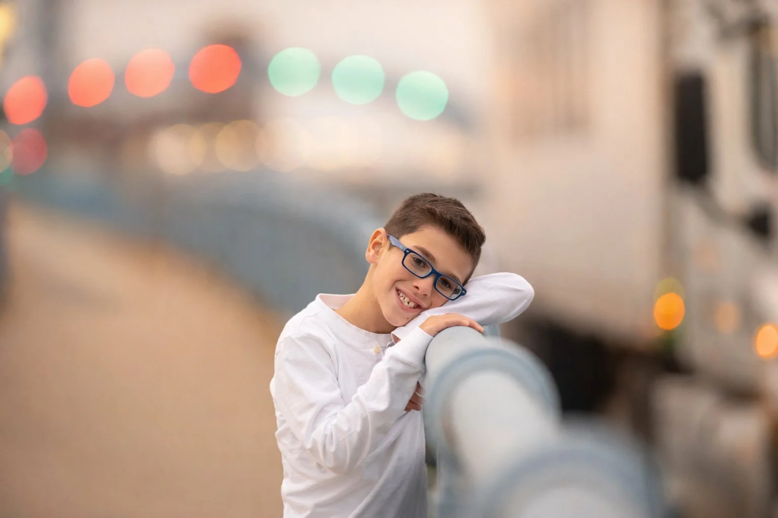 Boy leaning on a guardrail with soft bokeh lights behind him on the Benjamin Franklin Bridge in Philadelphia