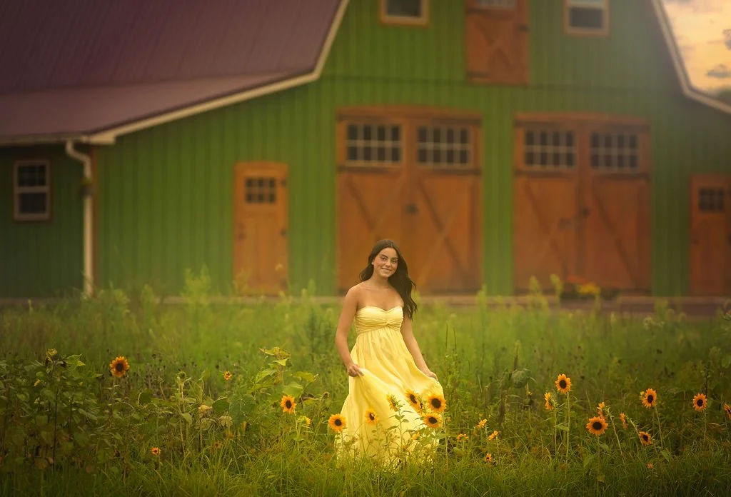 Teen girl in a yellow dress standing in a sunflower field near a rustic barn during a South Jersey senior portrait session.
