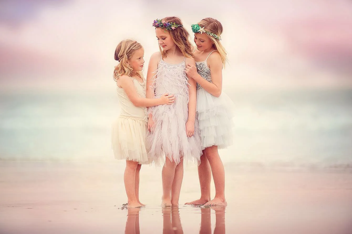 Three friends wearing pastel dresses standing together on the beach with the ocean in the background during a Jersey Shore portrait session