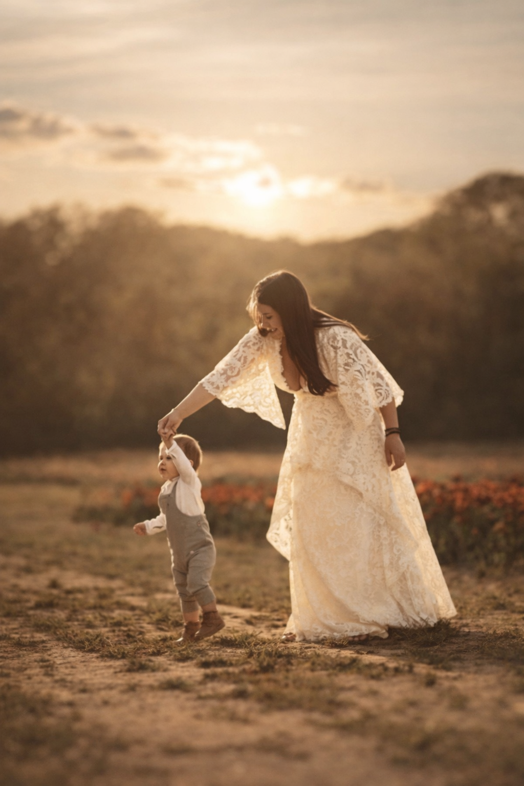 Mother guiding her toddler through a field during a fine art family photography session in warm golden hour light