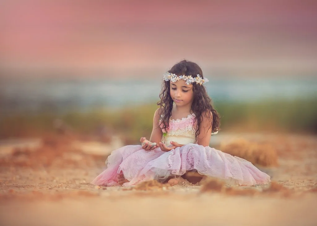 Close-up of a little girl holding seashells on the beach at Cape May, Jersey Shore, with a serene expression capturing the coastal beauty of her portrait session.