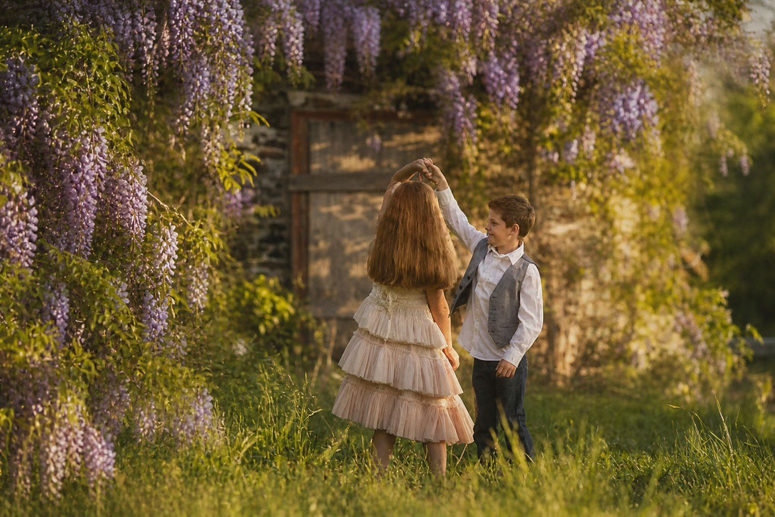 Brother and sister sharing one last twirl beneath blooming wisteria during a spring portrait session in South Jersey
