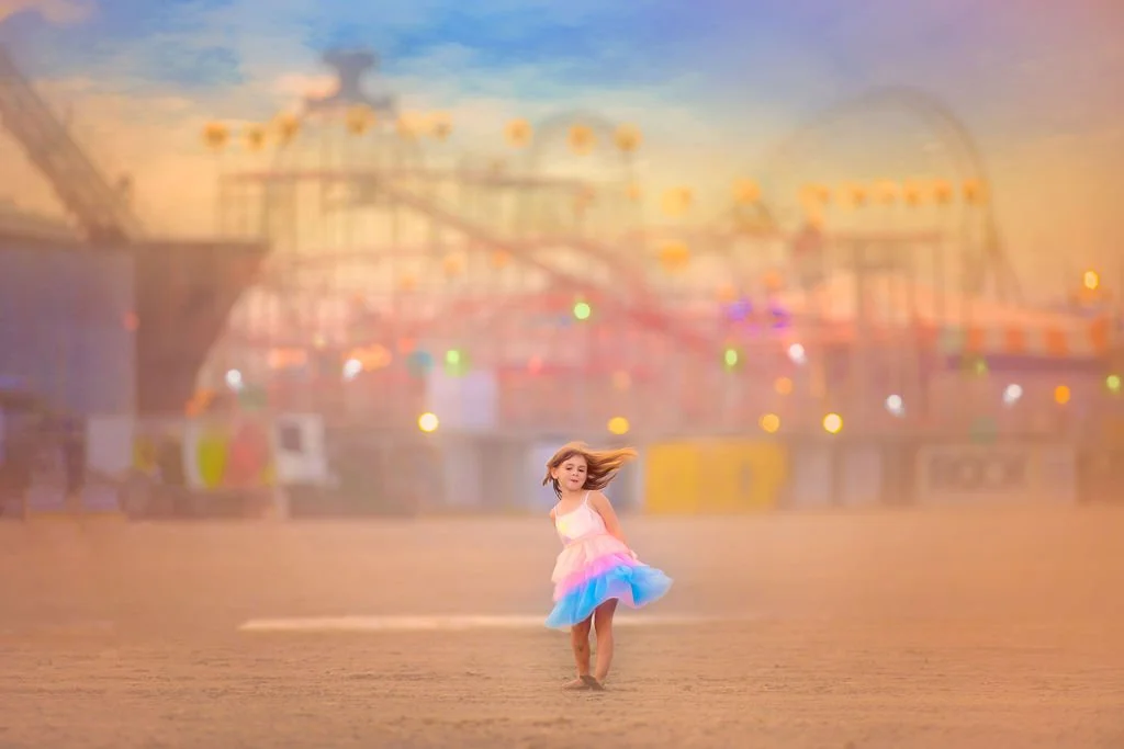 Girl twirling on the beach in Wildwood, NJ, wearing a rainbow-colored outfit with a roller coaster in the background.