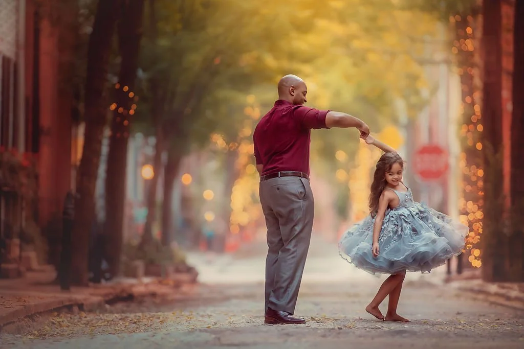 Father twirling his daughter during a joyful family portrait session on Addison Street in Philadelphia.