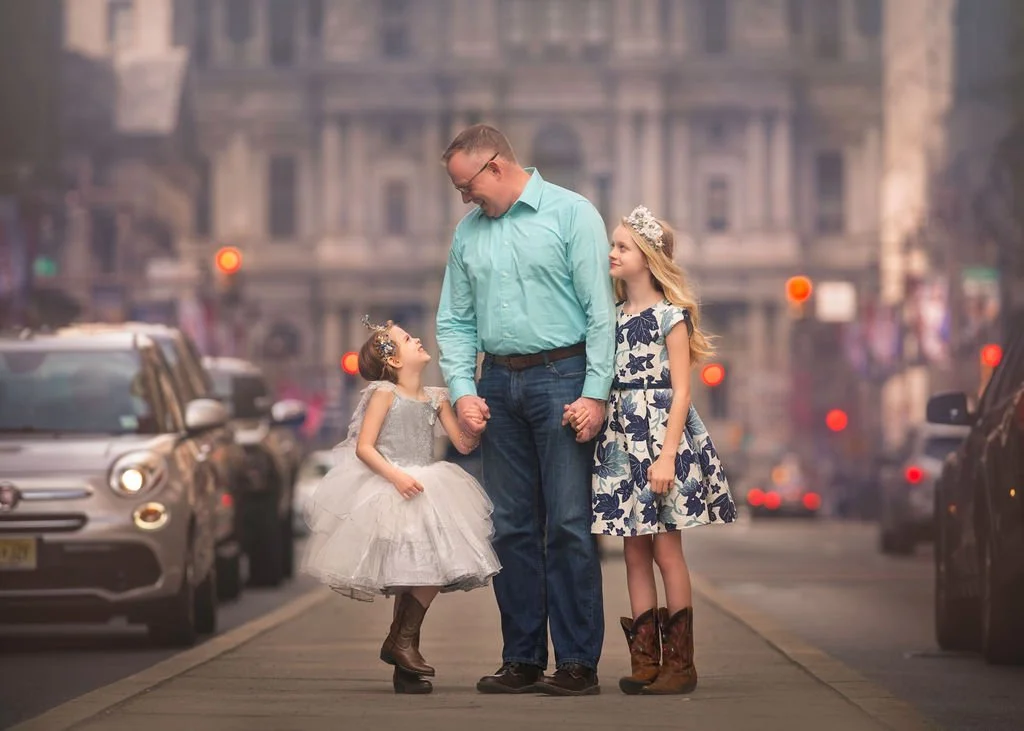 A father standing with his two daughters during a family portrait session on Broad Street in Philadelphia.