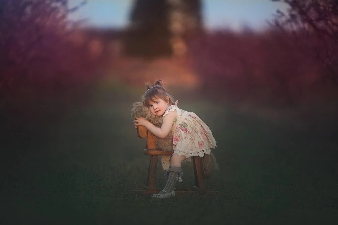Toddler sitting in an orchard holding a stuffed bear during a gentle, natural light baby and toddler portrait session in South Jersey.