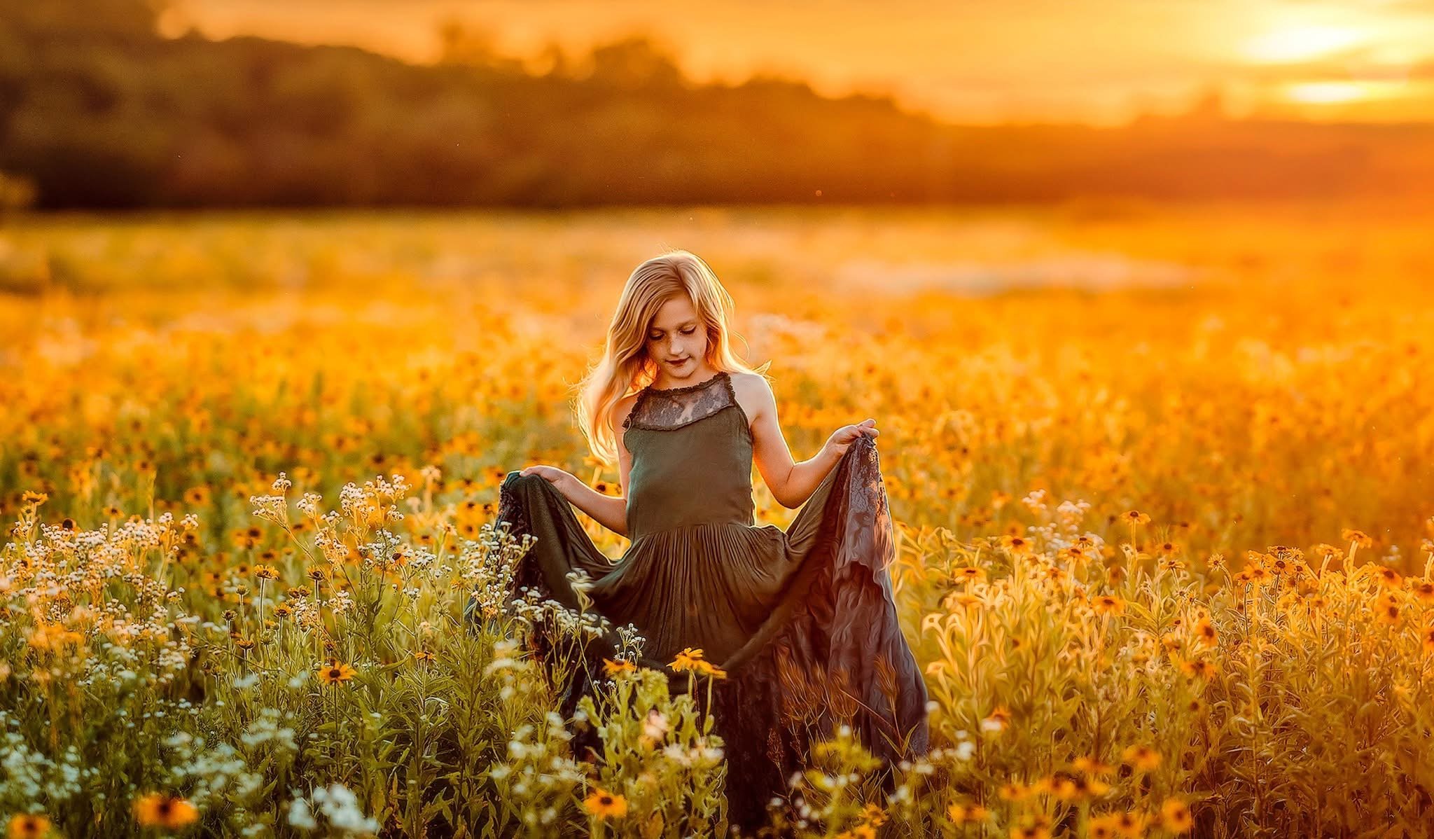 A fine art portrait of a young girl moving through a sun-drenched field at golden hour, surrounded by warm tones and natural light. The scene captures quiet emotion and the beauty of childhood through soft movement, texture, and an ethereal, painterl