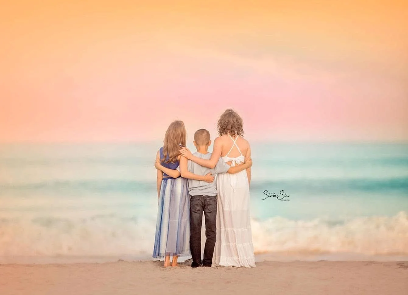 Three siblings looking out at the ocean during sunset in a Cape May family portrait session