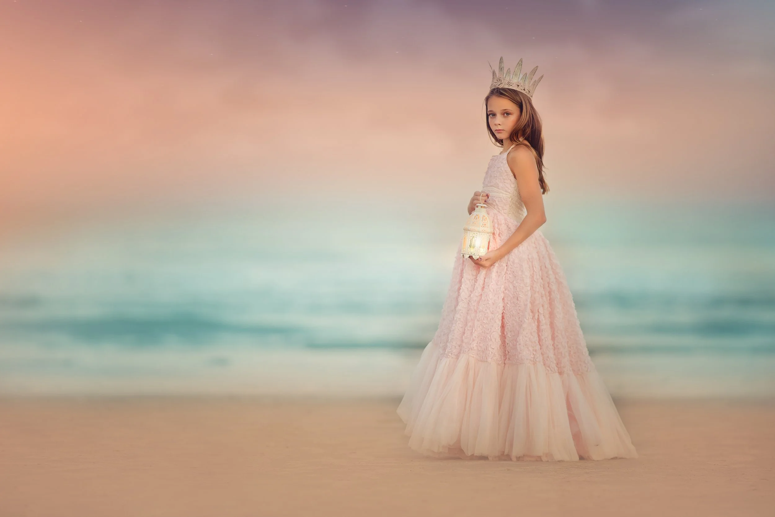 Girl in a long pink dress holding a lantern and wearing a crown during a beach portrait session in Wildwood New Jersey photographed by a Jersey Shore photographer.