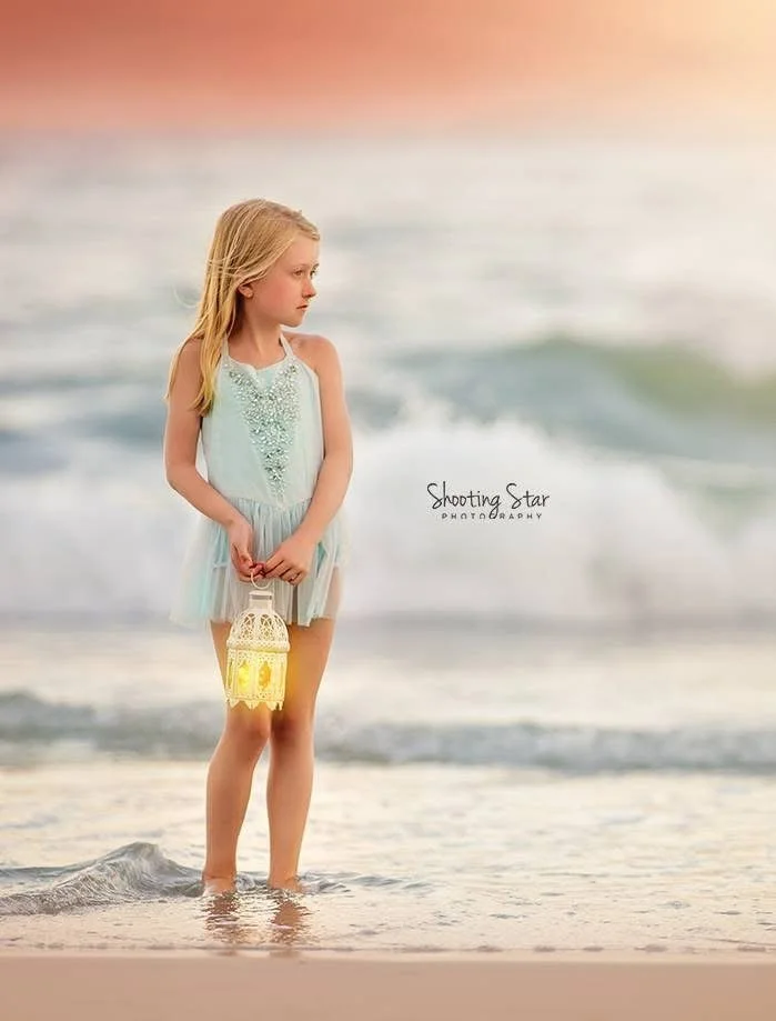 Young girl holding a lantern while looking out at the ocean during sunset in a Cape May family portrait session