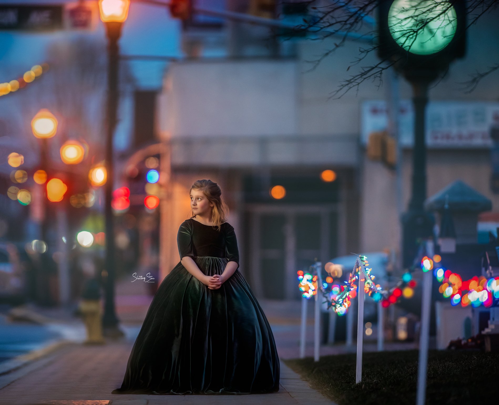 Child in elegant green dress standing on a sidewalk in downtown Pitman NJ with glowing street lights at dusk