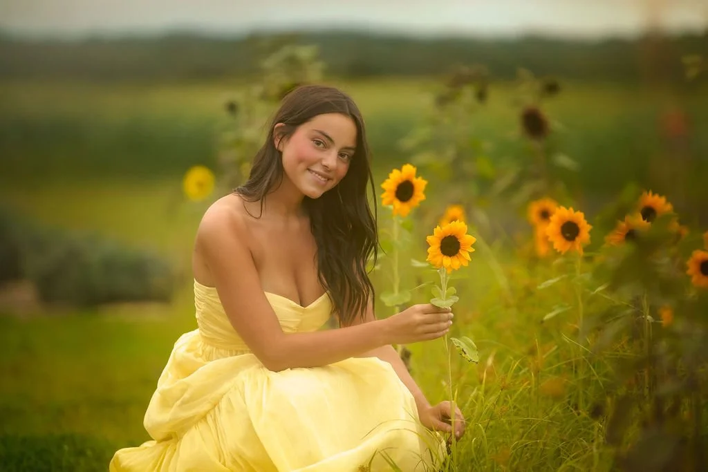 Teen girl holding a sunflower during an outdoor senior portrait session near Philadelphia with warm natural light.