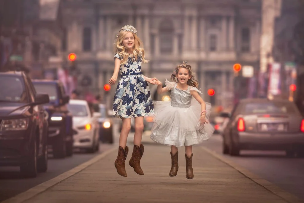 Two girls jumping and laughing together during a family portrait session on Broad Street in Philadelphia.